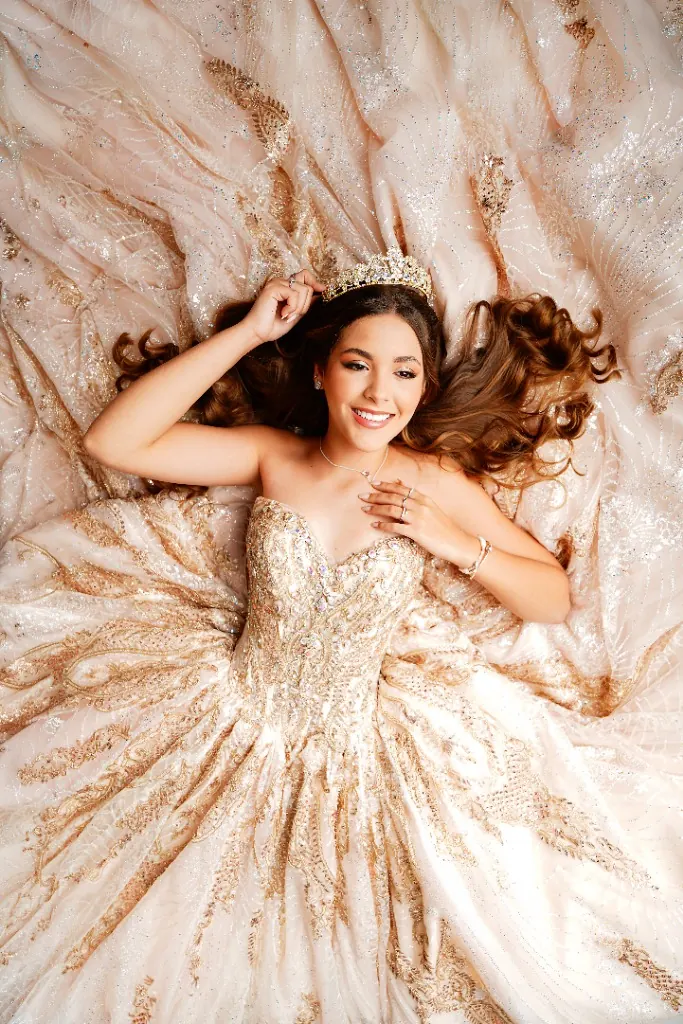 Debutante deitada em vestido de baile dourado e coroa, cabelo espalhado — ensaio de 15 anos em Brasília