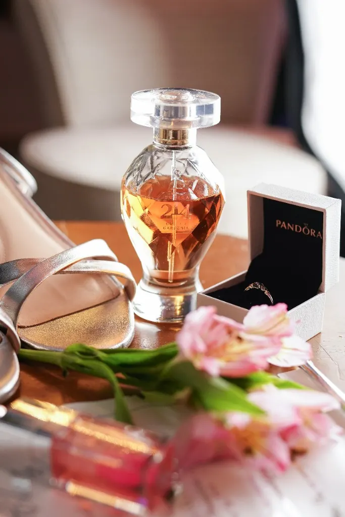 Detalhes do dia: perfume, sandália prata, anel e flores sobre a mesa — ensaio de 15 anos em Brasília