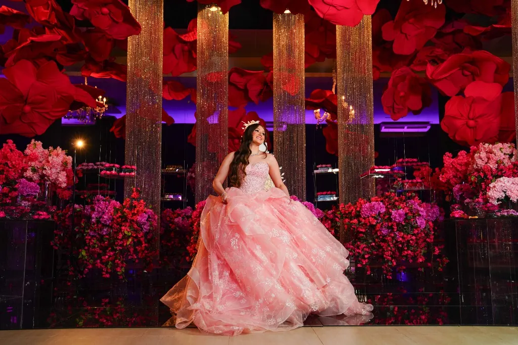 Debutante em vestido rosé sentada na decoração de flores e colunas douradas — festa de 15 anos em Brasília