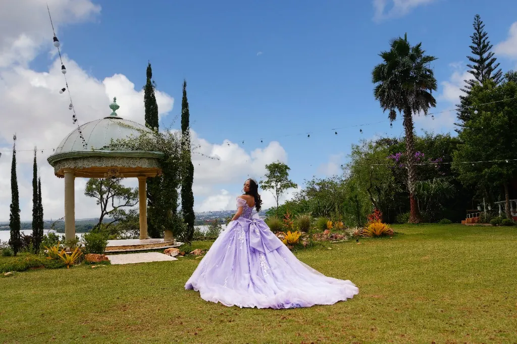 Debutante em vestido lilás num jardim com coreto e vista do lago — ensaio de 15 anos ao ar livre em Brasília