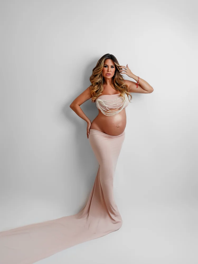 Gestante em vestido rosé de perfil, cauda do vestido esvoaçante — ensaio gestante em estúdio