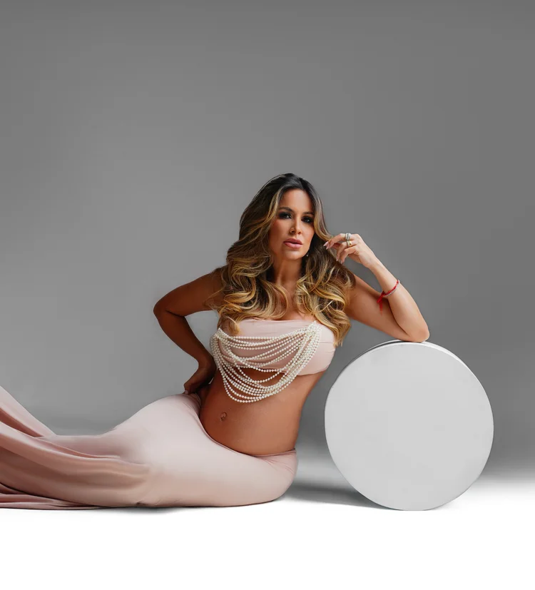 Gestante apoiada em prop redondo branco, vestido rosé com pérolas — ensaio gestante em estúdio