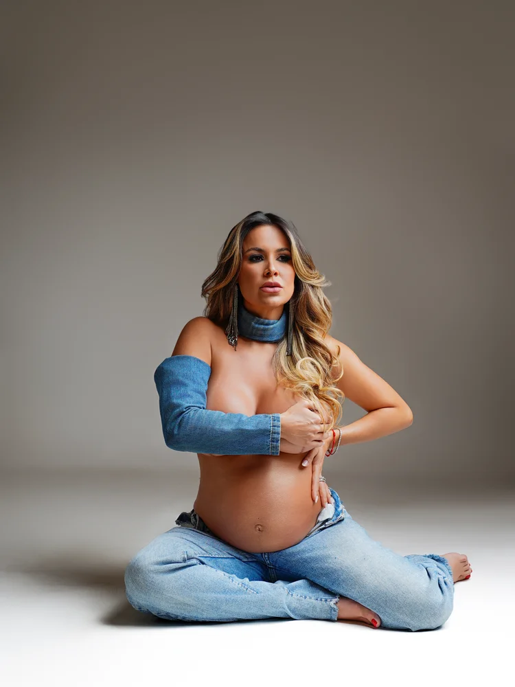 Gestante em jaqueta jeans, sentada na cadeira de diretor — ensaio gestante em estúdio