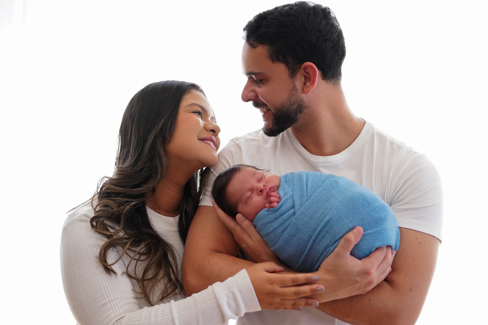 Mãe olhando para o pai, sorrindo, enquanto seguram o recém-nascido em manta azul