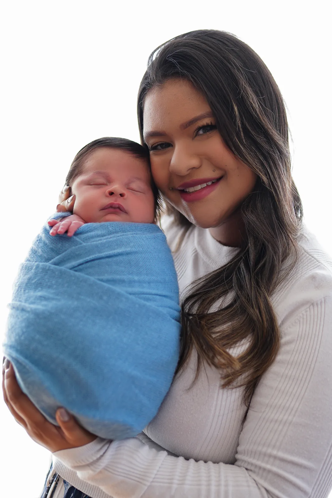 Mãe sorridente com o recém-nascido no colo, manta azul, olhando para a câmera