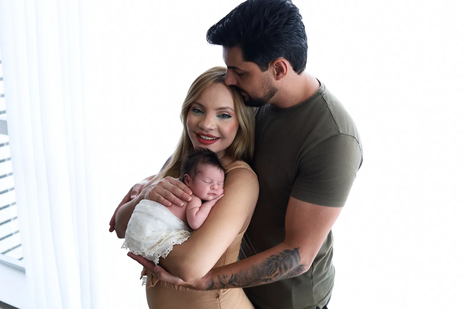 Pai beijando a testa da mãe com a bebê no colo, outro ângulo