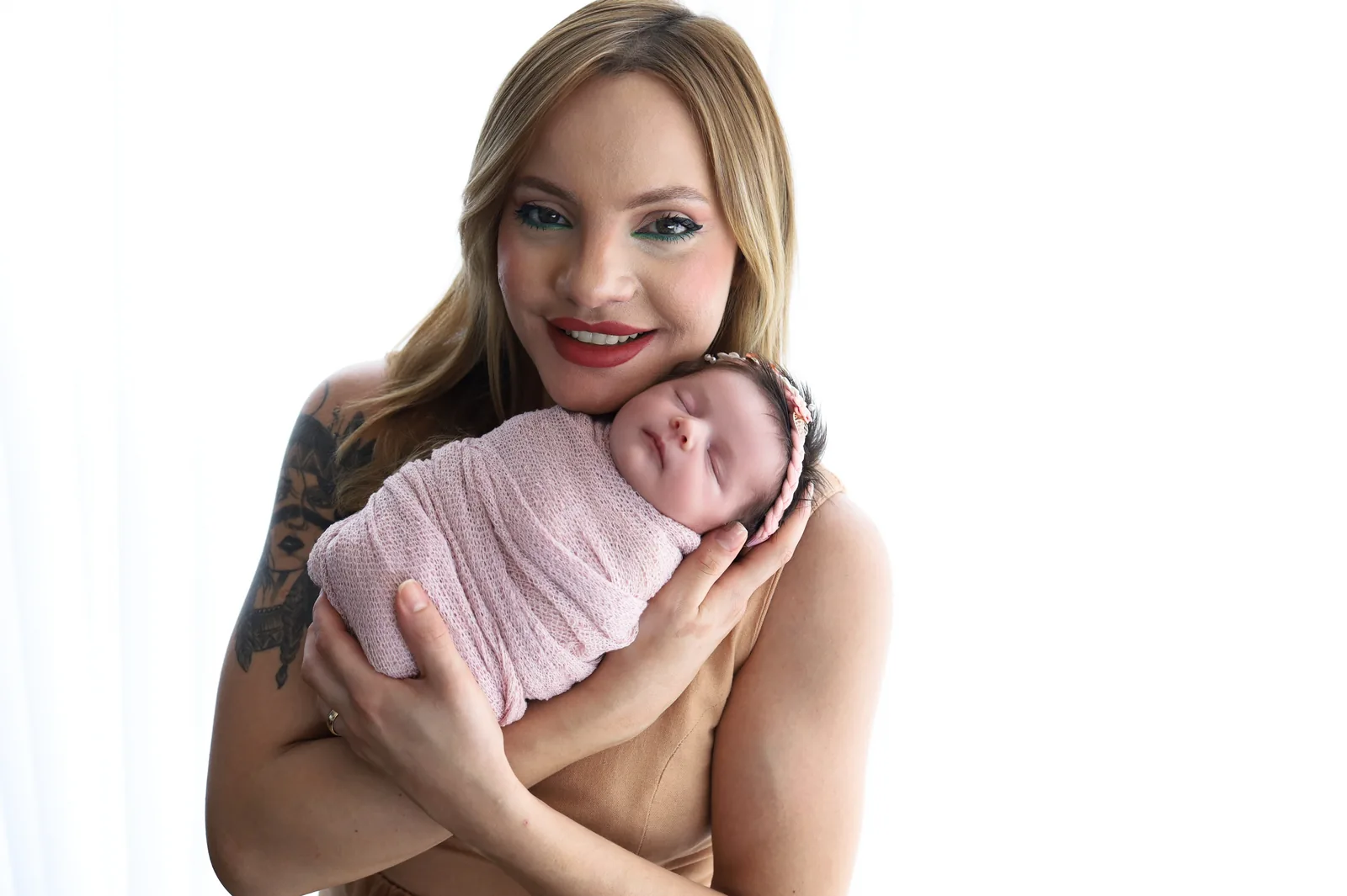 Mãe com a recém-nascida no colo, manta rosa, olhando para a câmera de perto