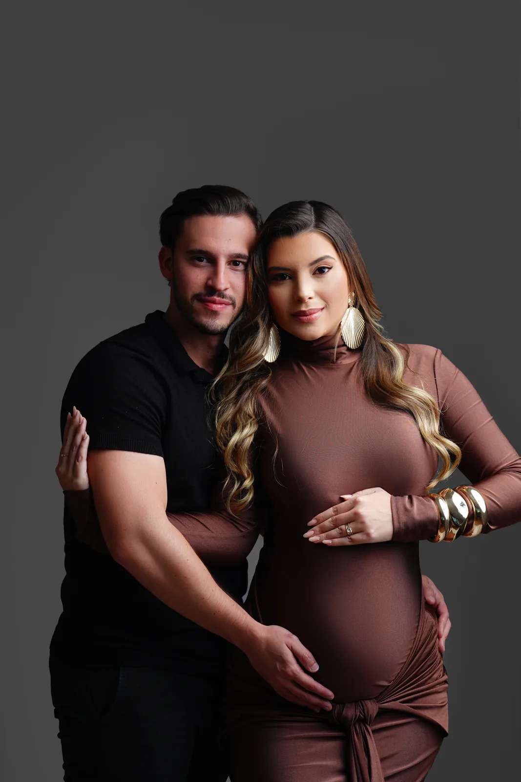 Casal grávido em retrato de perto, brincos de concha dourados, vestido marrom