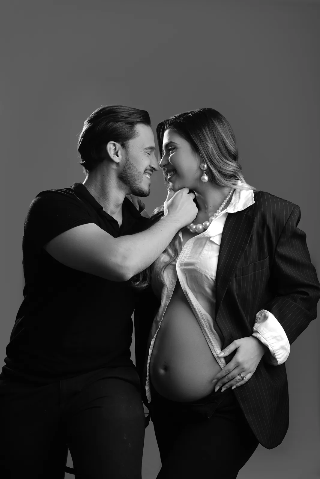Casal grávido, blazer e colar de pérolas, mesma cena em preto e branco