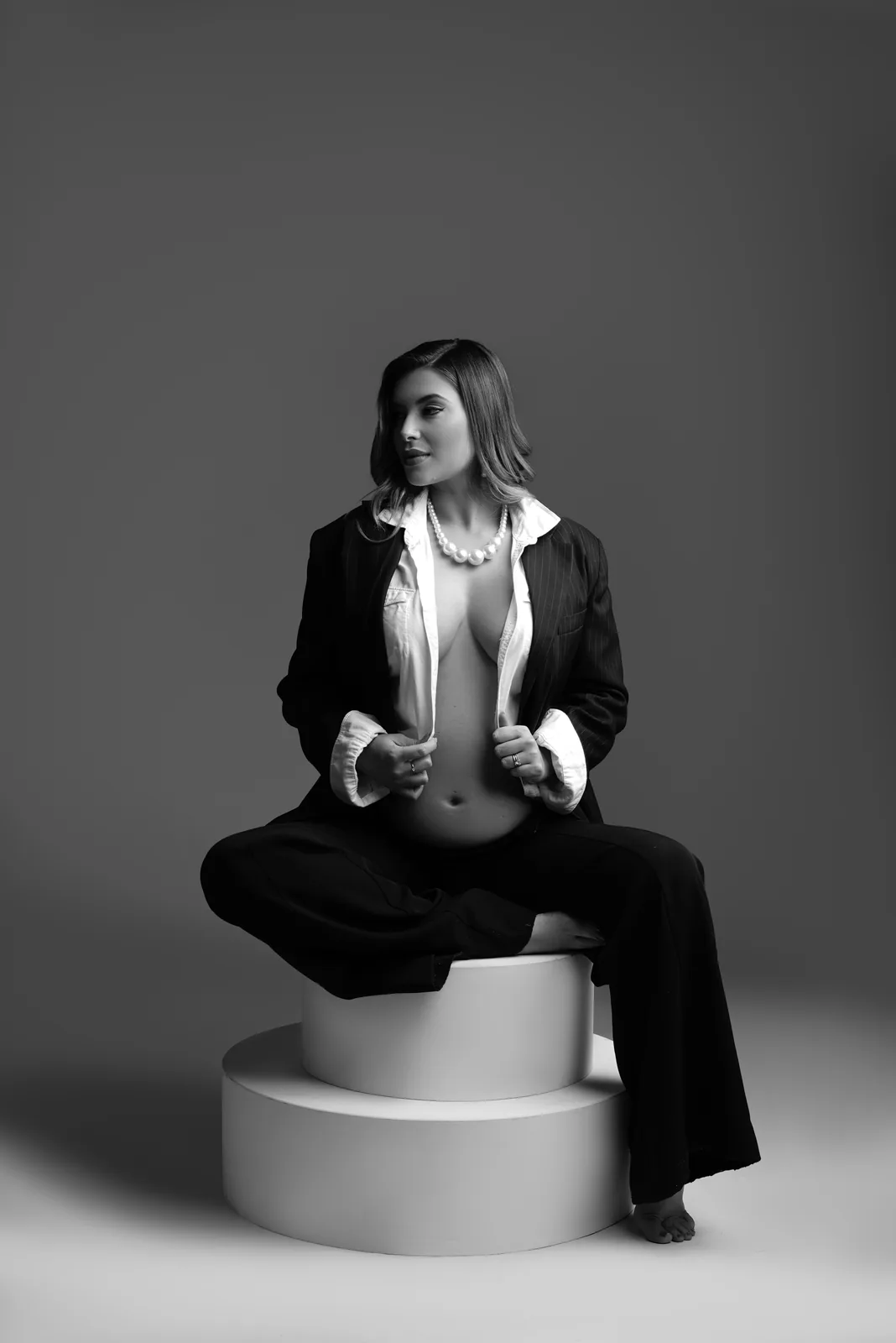 Gestante sentada em cubo branco, blazer, mesma cena em preto e branco