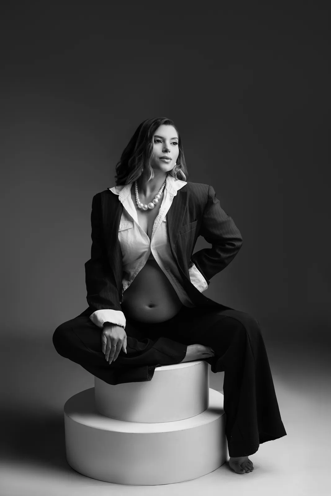 Gestante sentada em pedestal, blazer e colar de pérolas, mesma cena em preto e branco