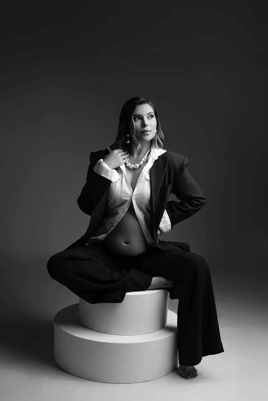Gestante sentada em pedestal, mão no colar, mesma cena em preto e branco