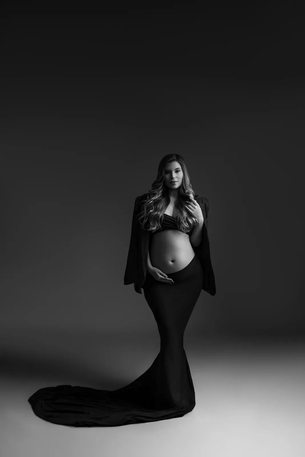 Gestante em vestido preto sereia, mão na barriga, mesma cena em preto e branco