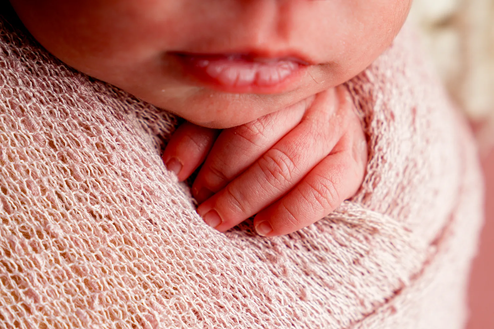 Mão da recém-nascida apoiada perto do queixo, detalhe de perto, manta rosa
