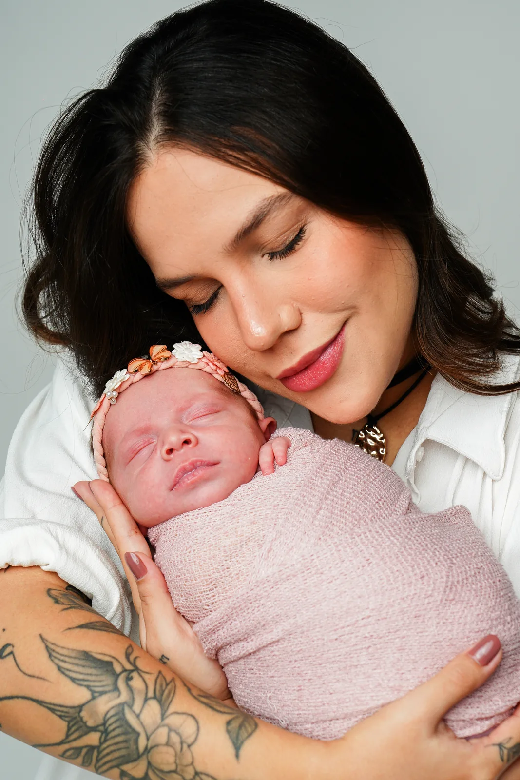 Mãe olhando para a filha recém-nascida no colo, sorrindo, manta rosa