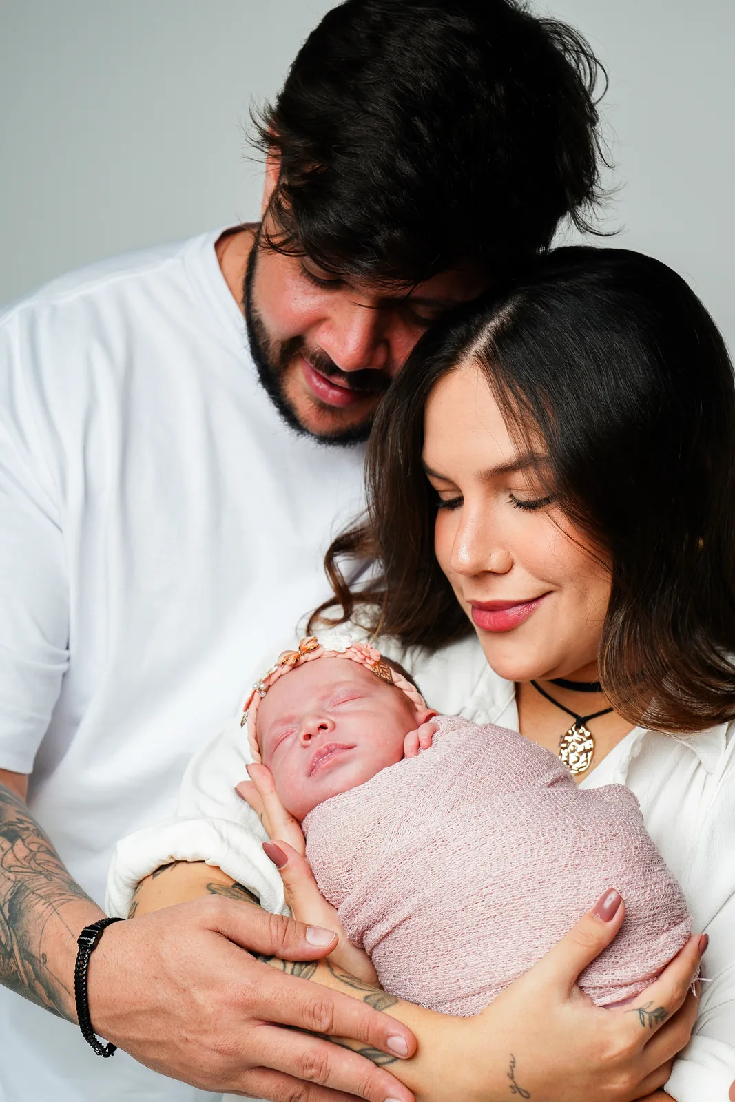 Pai e mãe segurando a recém-nascida juntos, ambos olhando para ela sorrindo