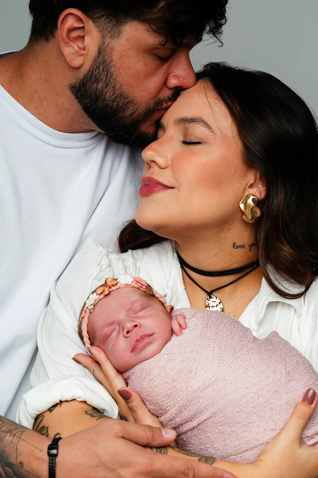 Pai beijando a testa da mãe, que segura a recém-nascida no colo