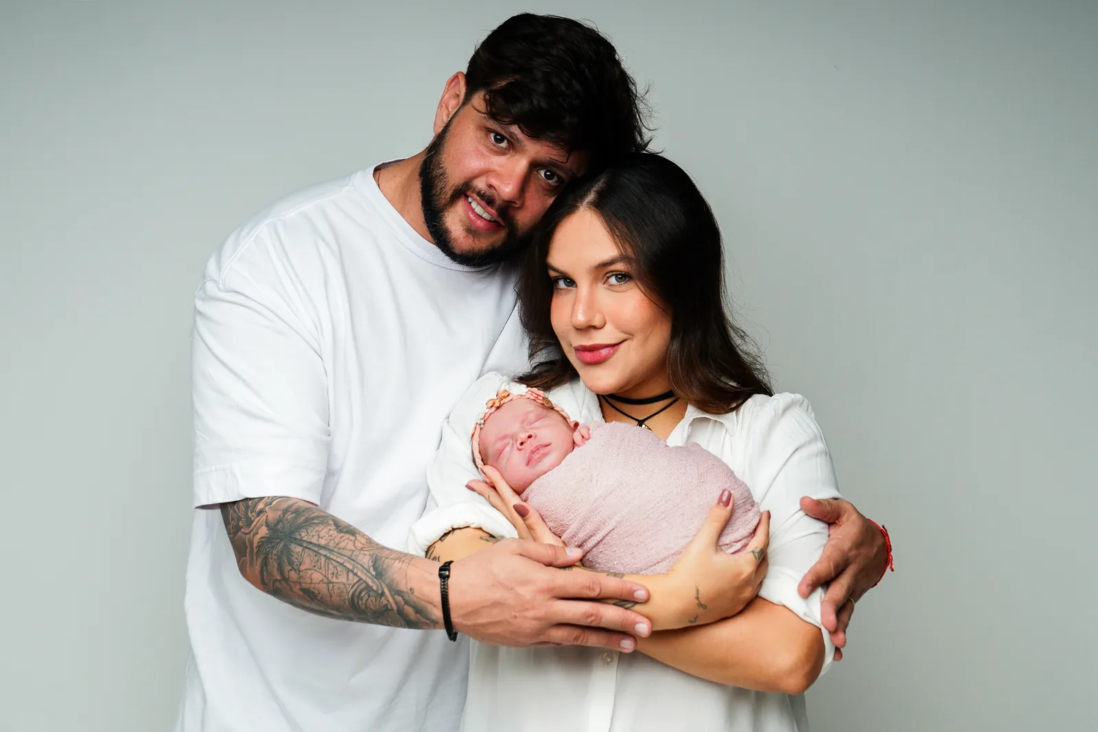 Família reunida — pai, mãe e recém-nascida, todos sorrindo para a câmera