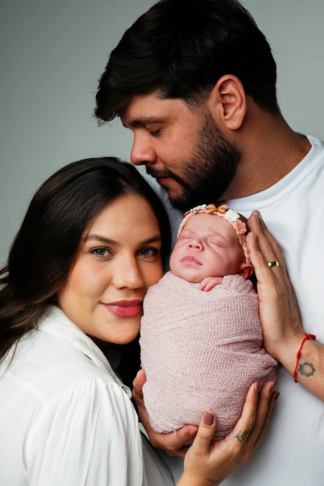 Pai e mãe com a recém-nascida no colo, retrato de perto, olhando para a câmera