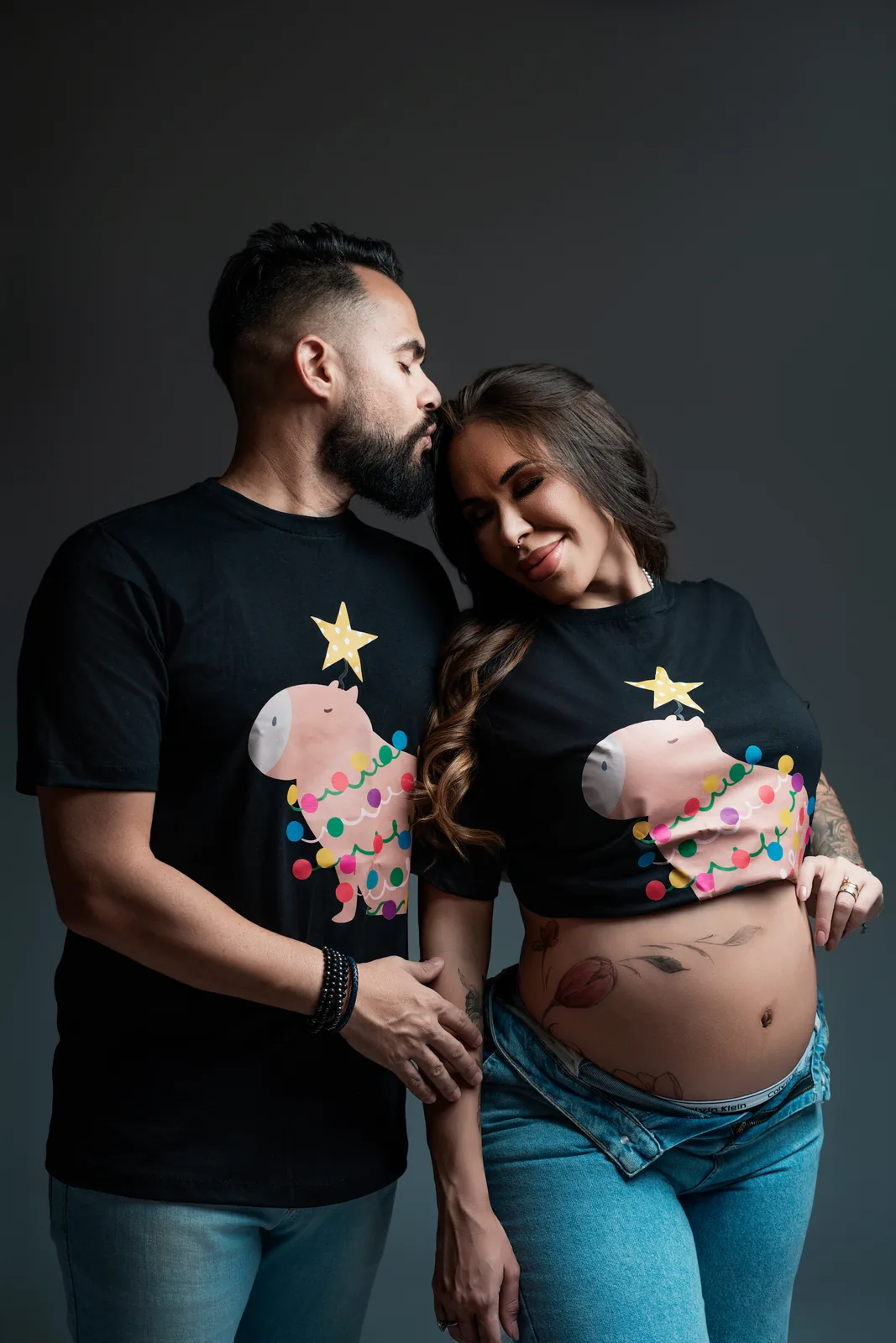 Família em camisetas natalinas combinando — marido, gestante e filha sorrindo