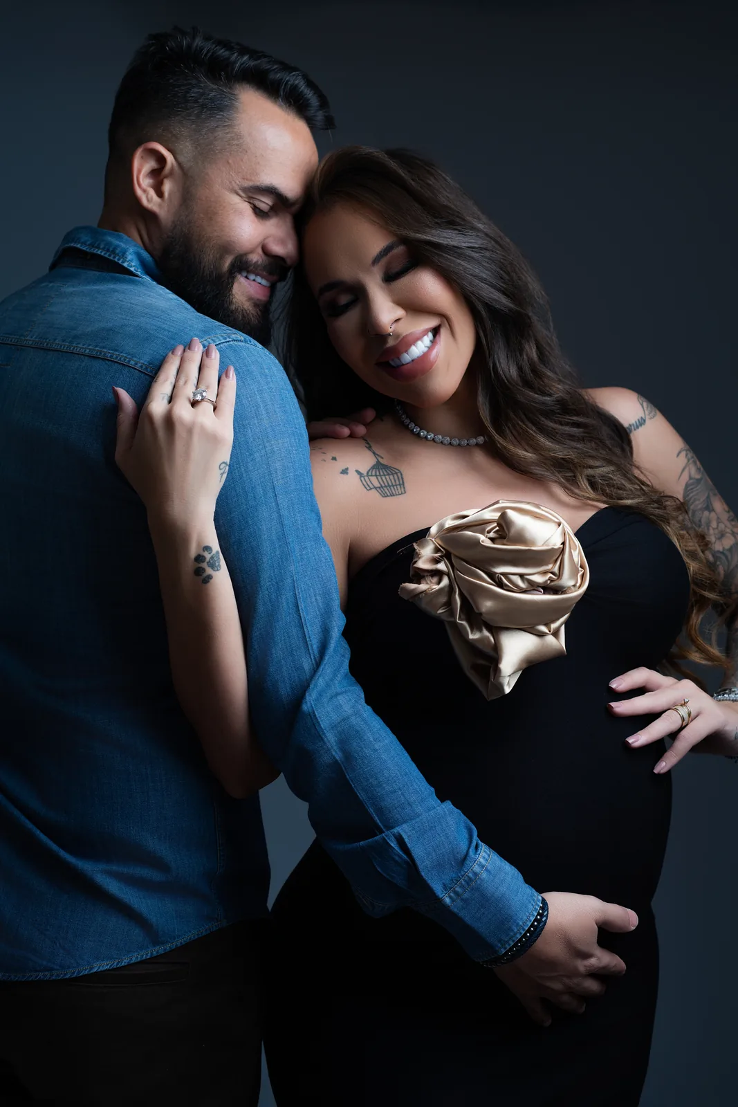 Gestante em manto preto com laço, pose ajoelhada, tatuagens na perna e no quadril