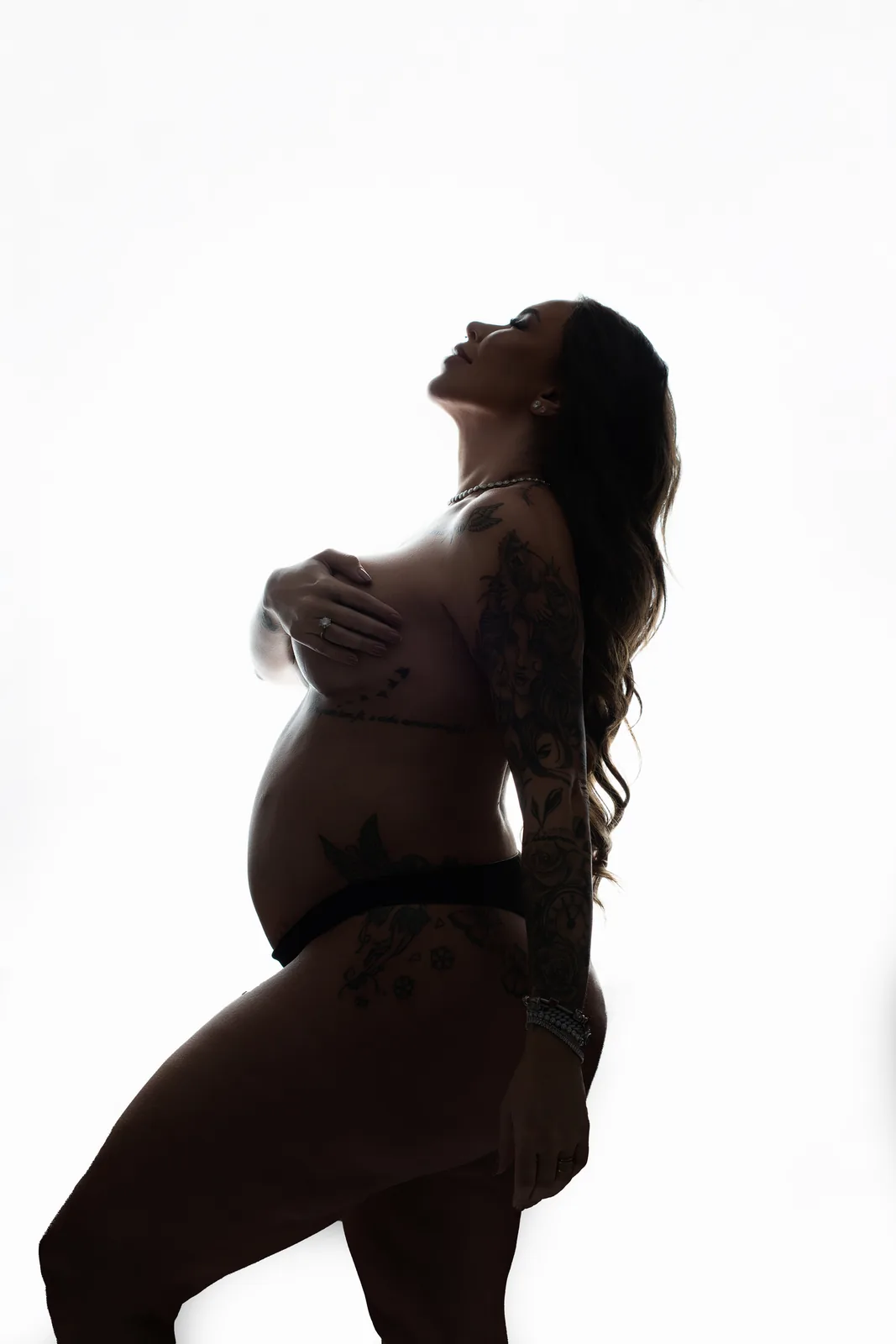 Casal grávido em silhueta contraluz, ele sem camisa, testas coladas, mãos na barriga