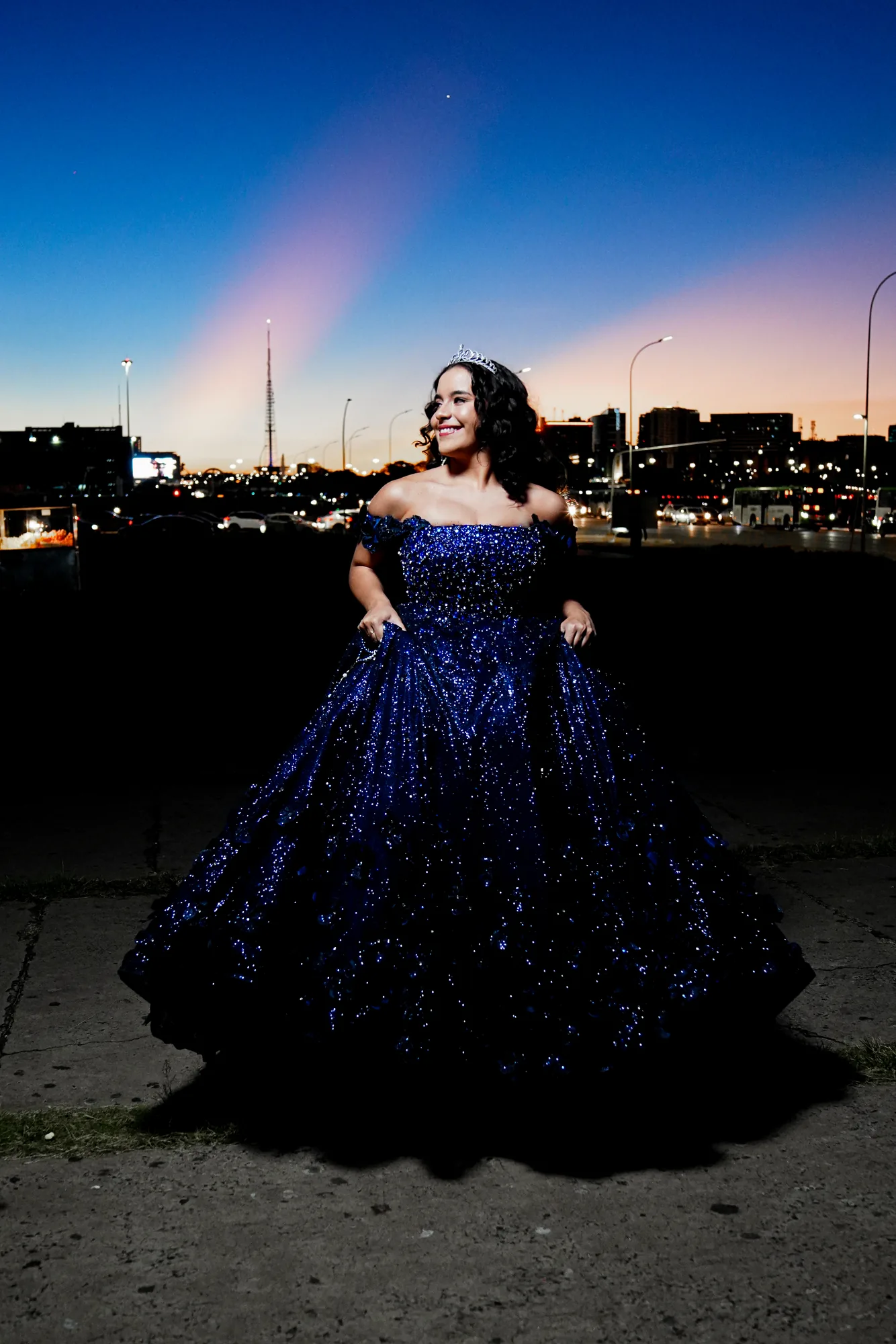 Debutante de vestido azul-marinho na Ponte JK ao entardecer, luzes da cidade desfocadas