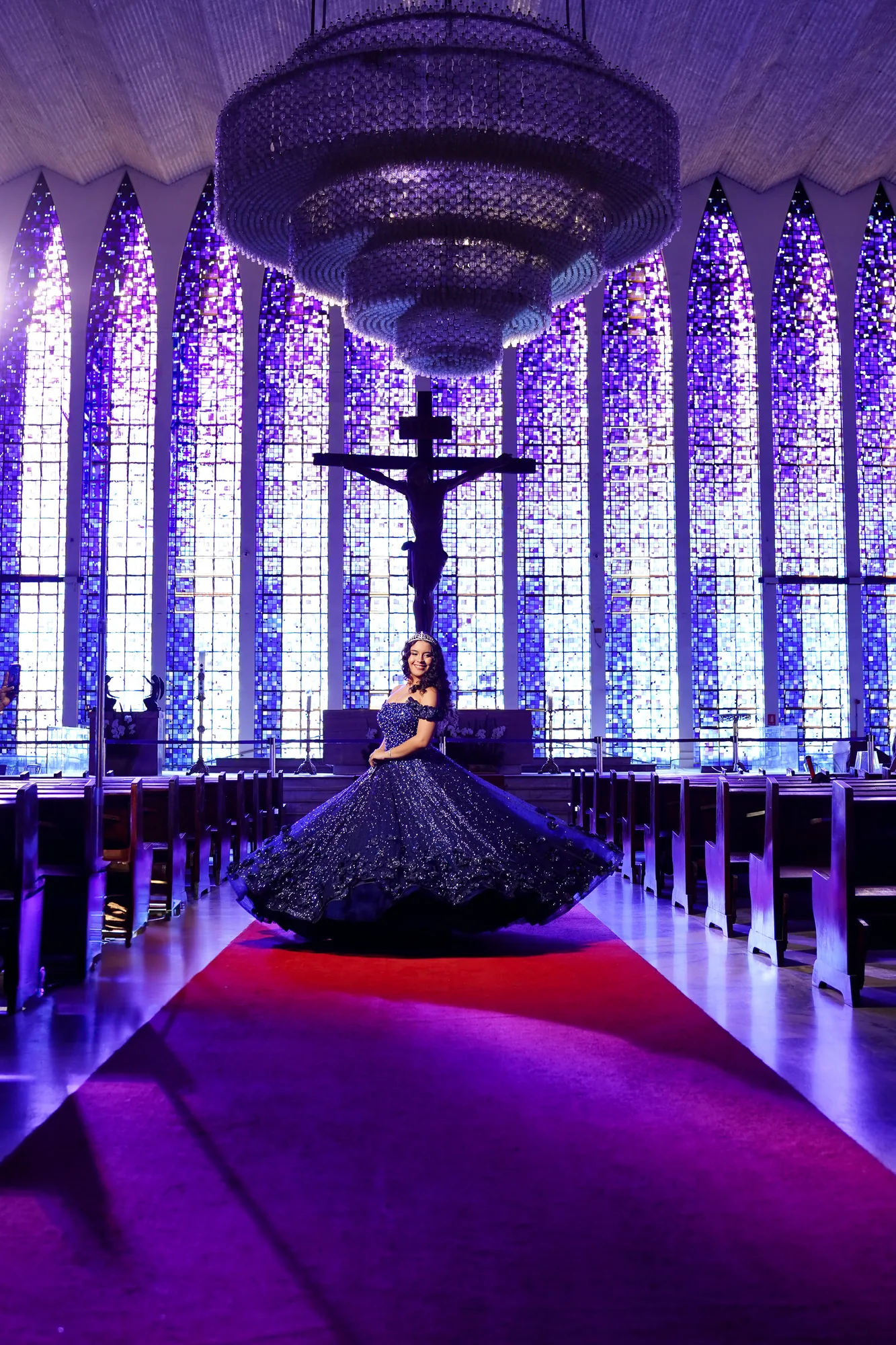 Debutante de vestido azul-marinho dentro da Catedral Metropolitana de Brasília, vitrais ao fundo