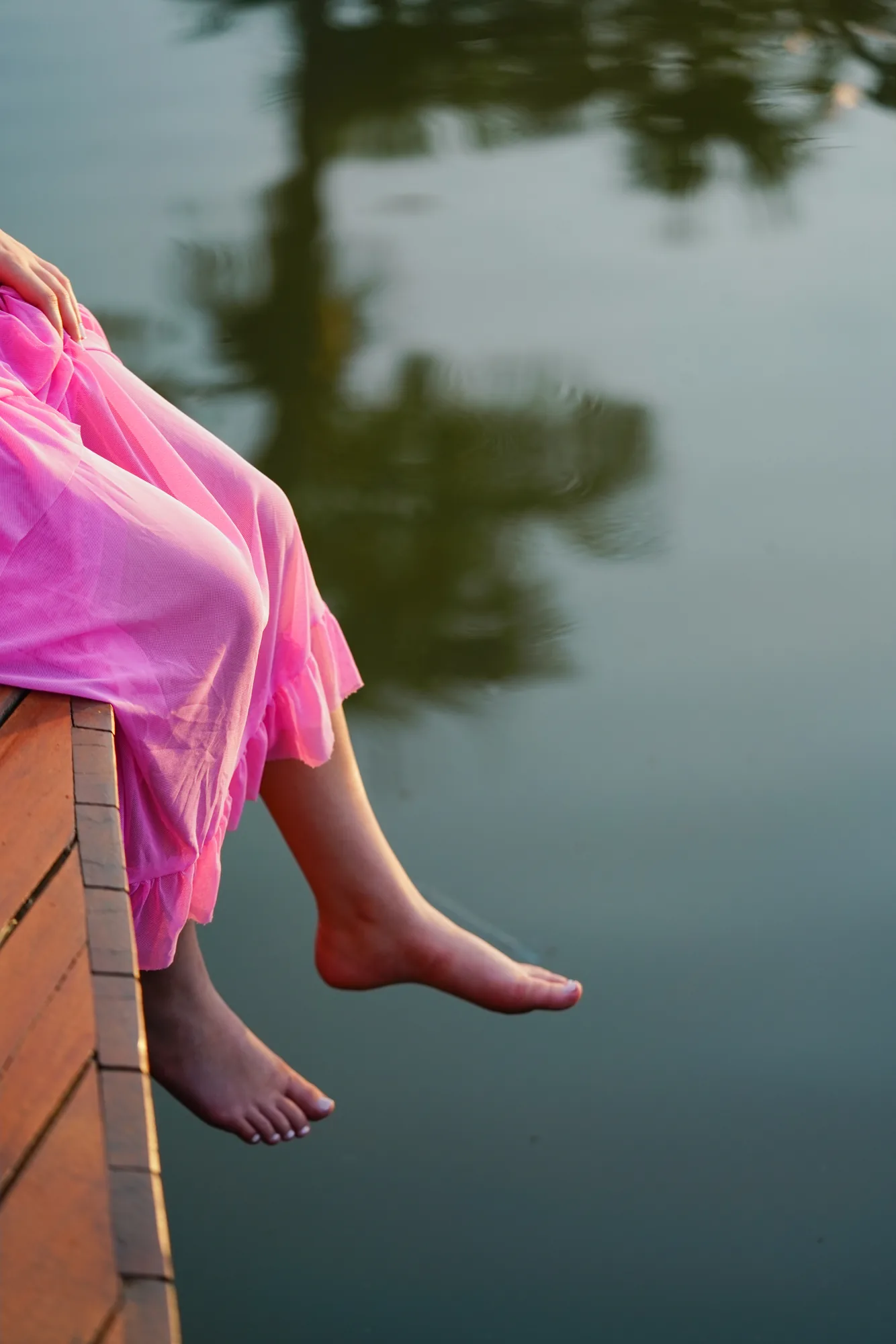 Debutante sentada no deck de madeira sobre o lago da Casa da Ana, pés à mostra