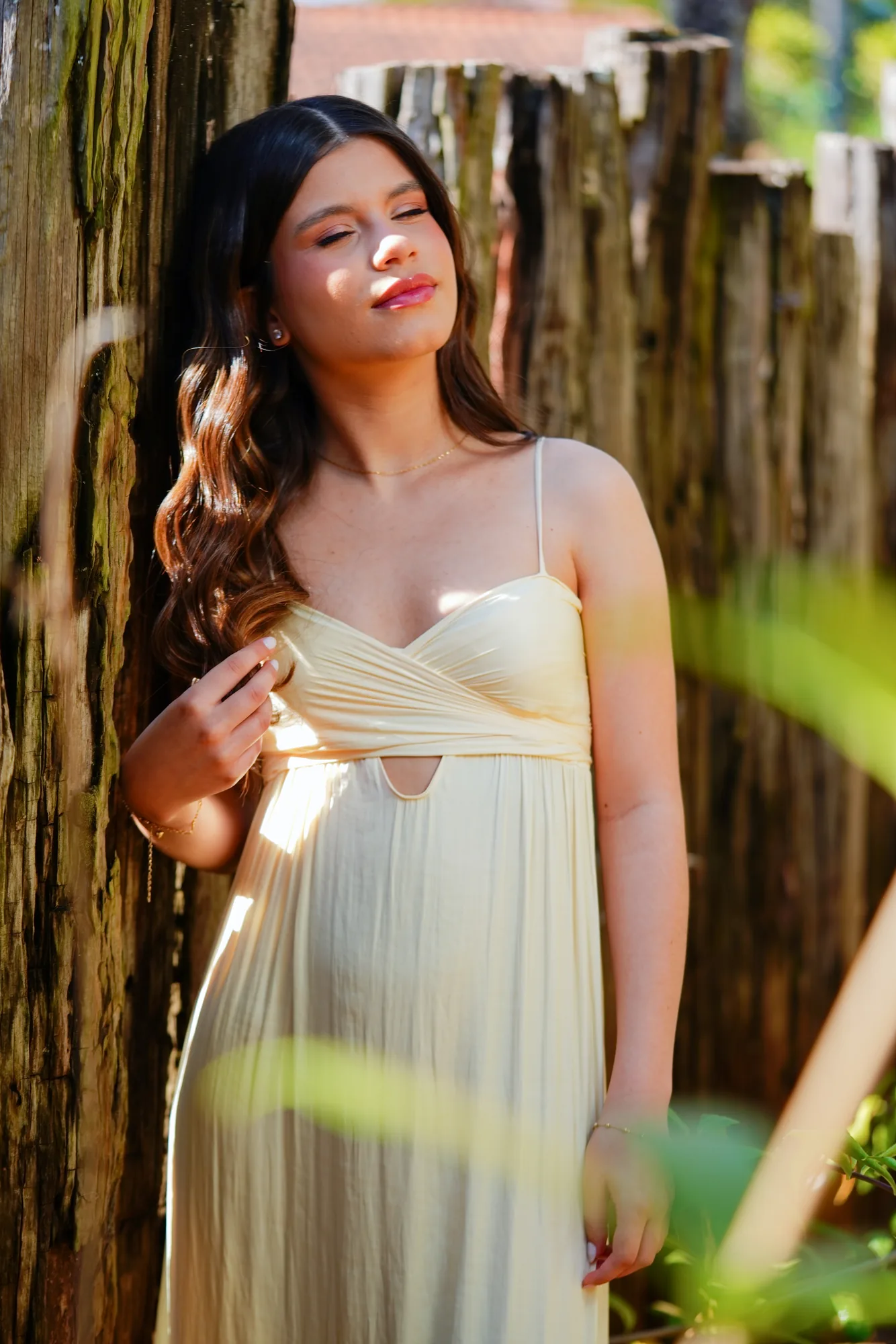 Debutante de vestido branco encostada em cerca de madeira, jardim da Casa da Ana