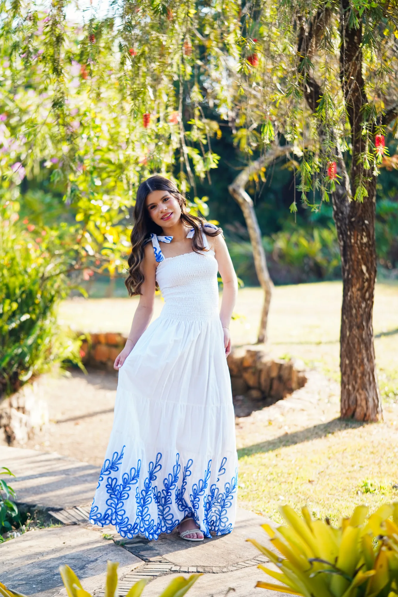 Debutante de vestido branco sentada no gramado sob as árvores da Casa da Ana