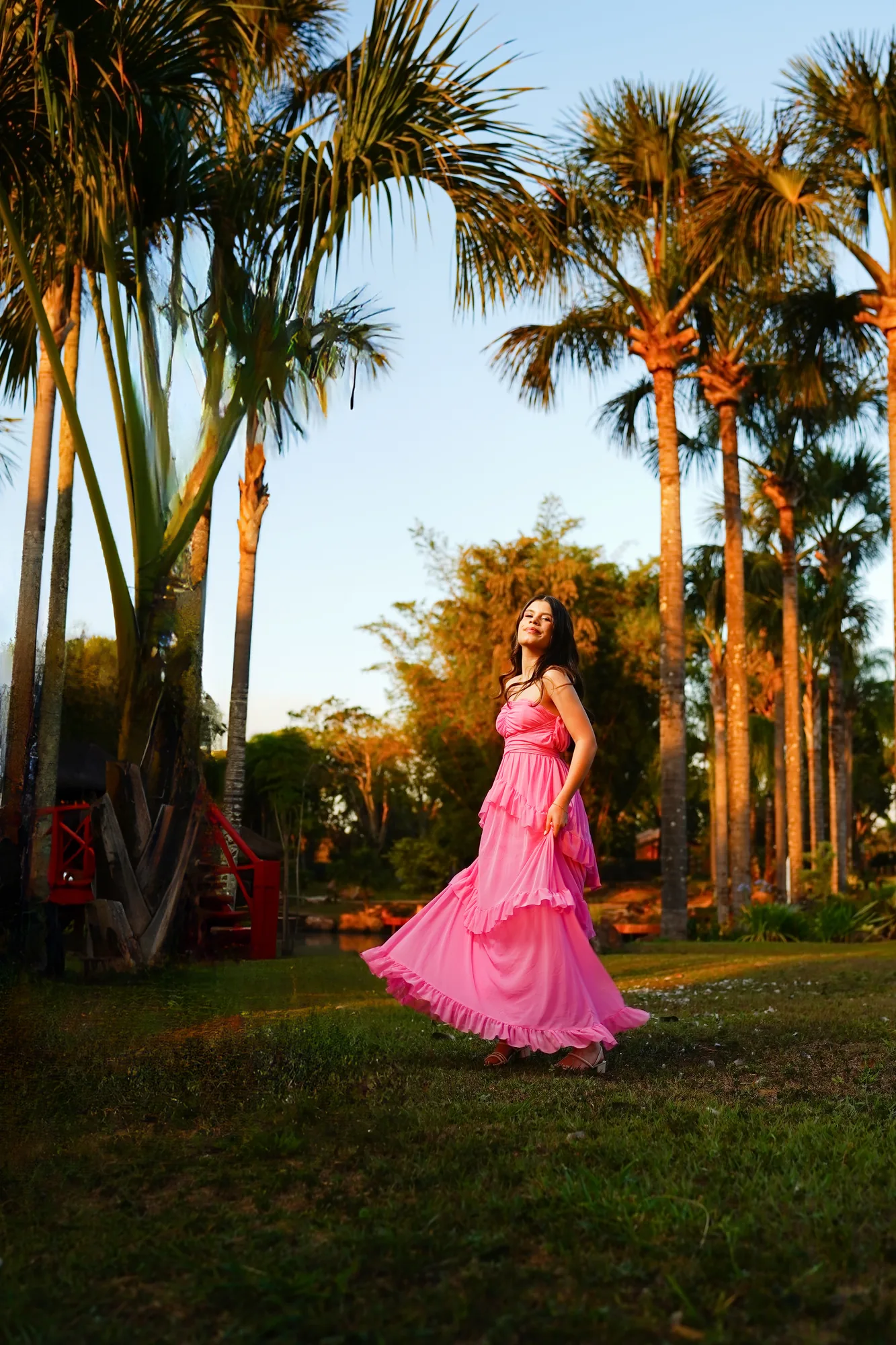 Debutante de vestido rosa correndo entre palmeiras douradas ao pôr do sol na Casa da Ana