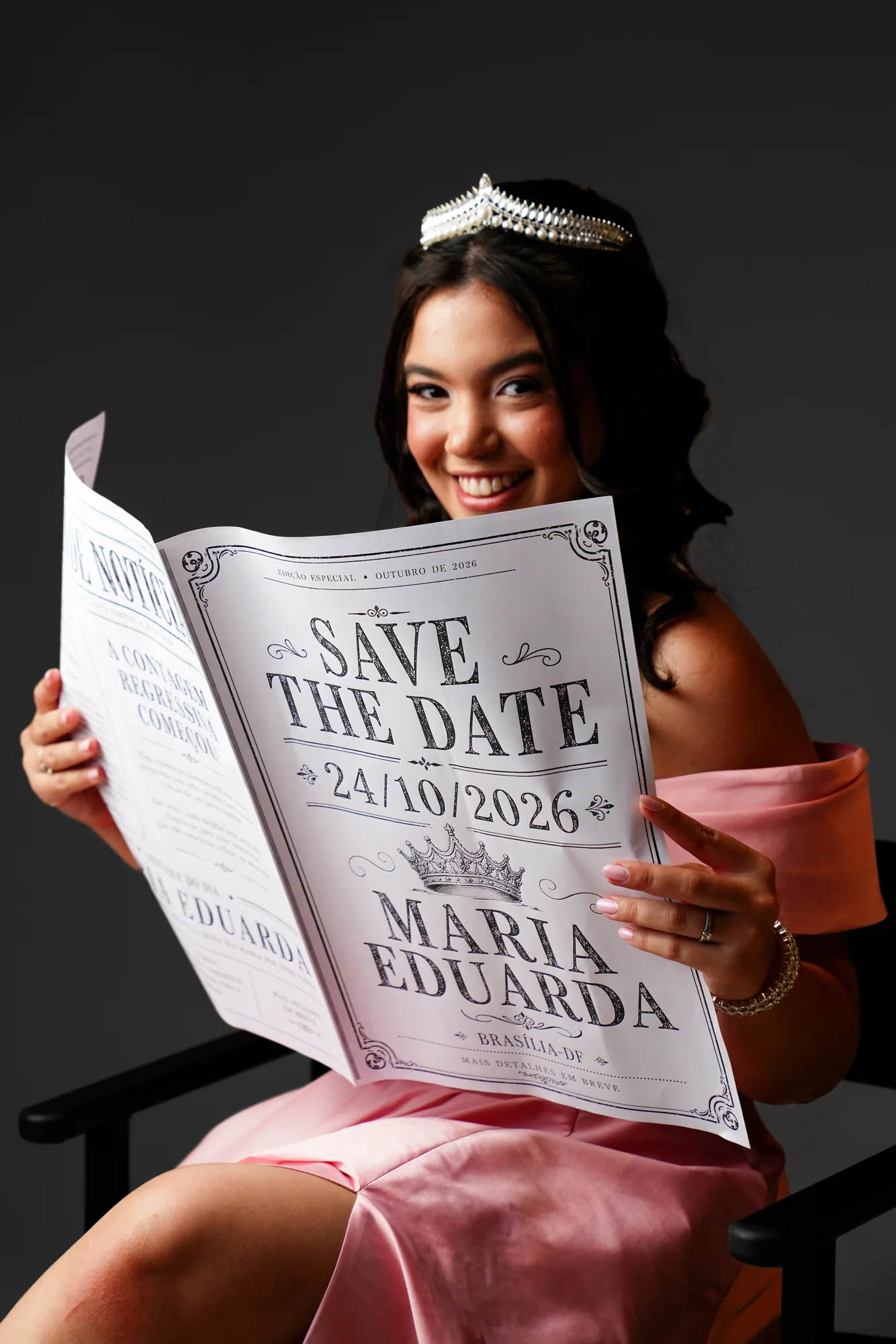 Debutante de vestido rosé lendo jornal com a notícia dos 15 anos, still em estúdio