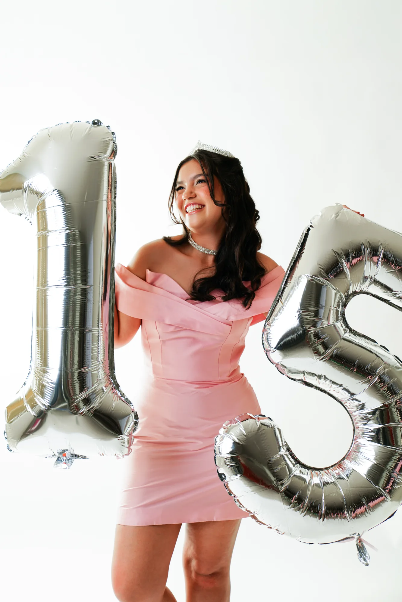 Debutante de vestido rosé ao lado de balões dourados formando o número 15, em estúdio