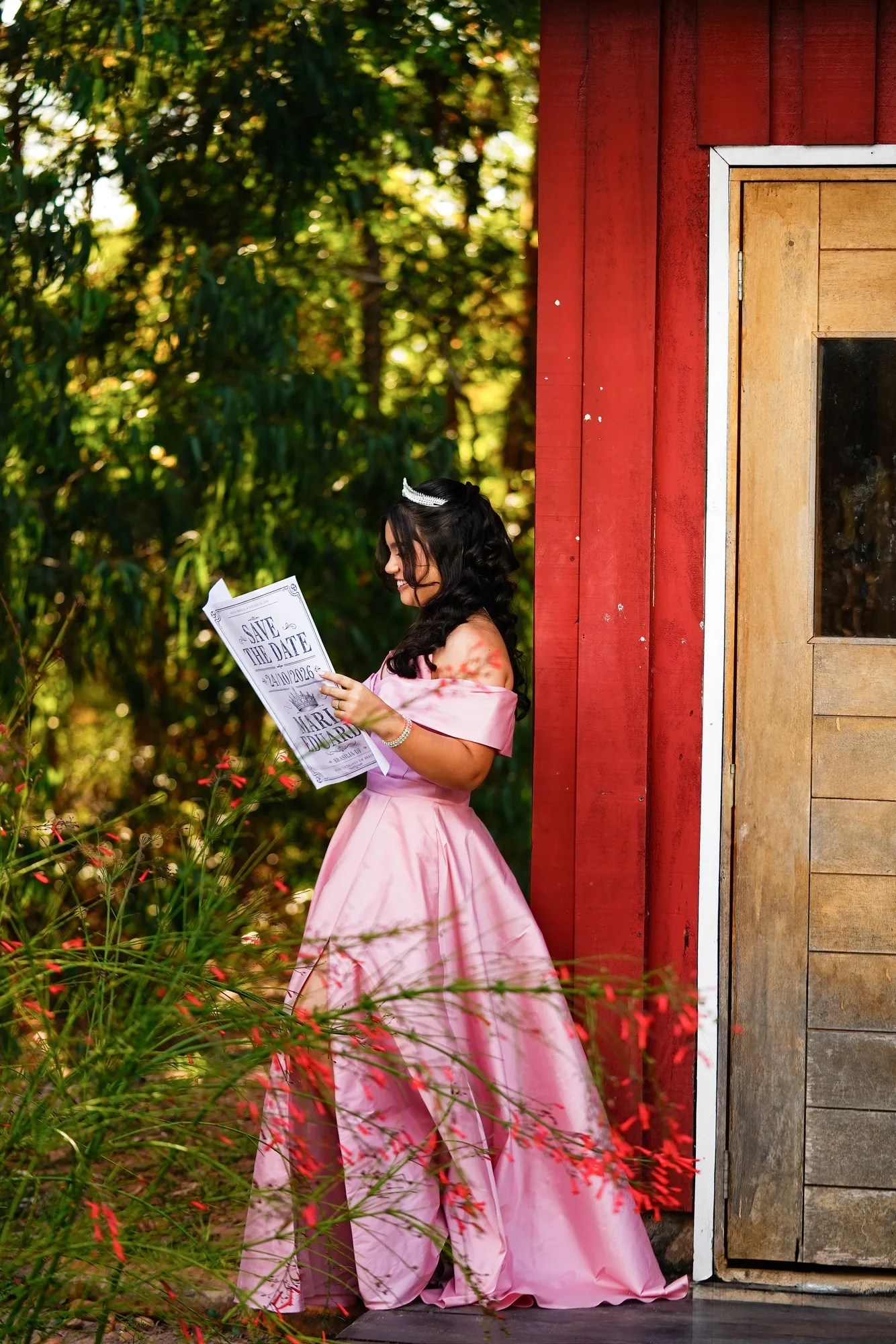 Debutante de vestido rosa lendo o save the date em frente a um casebre de madeira no Jardim Botânico de Brasília
