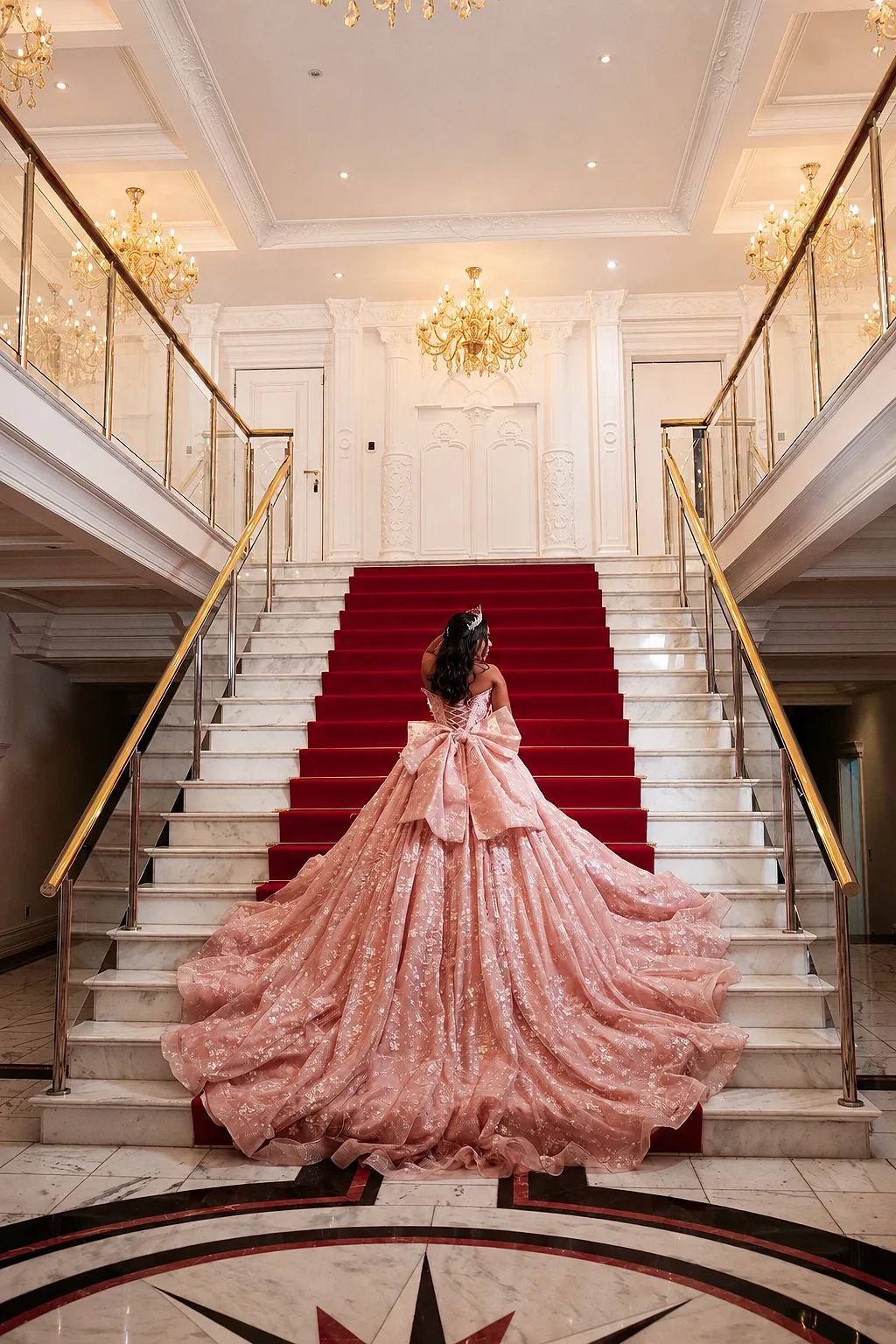 Debutante descendo a escadaria com tapete vermelho e lustre da Mansão Solêmio, vestido rosé