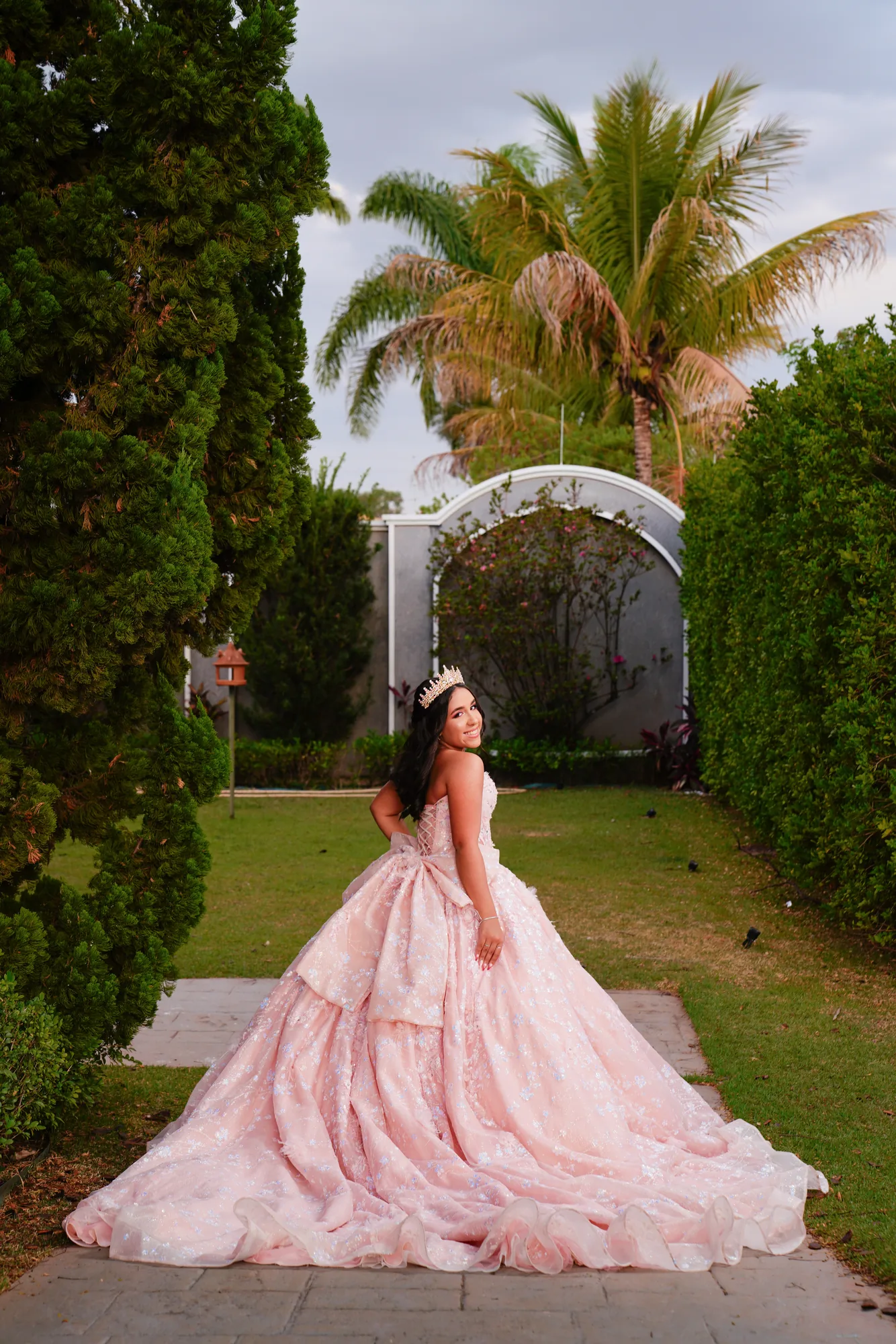 Debutante caminhando pelo jardim em frente à fachada da Mansão Solêmio, vestido rosé com cauda
