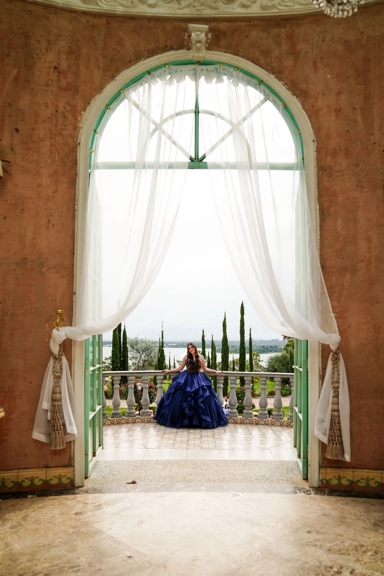 Debutante em pé sob o arco do jardim de inverno da Villa Giardini, vestido azul-marinho