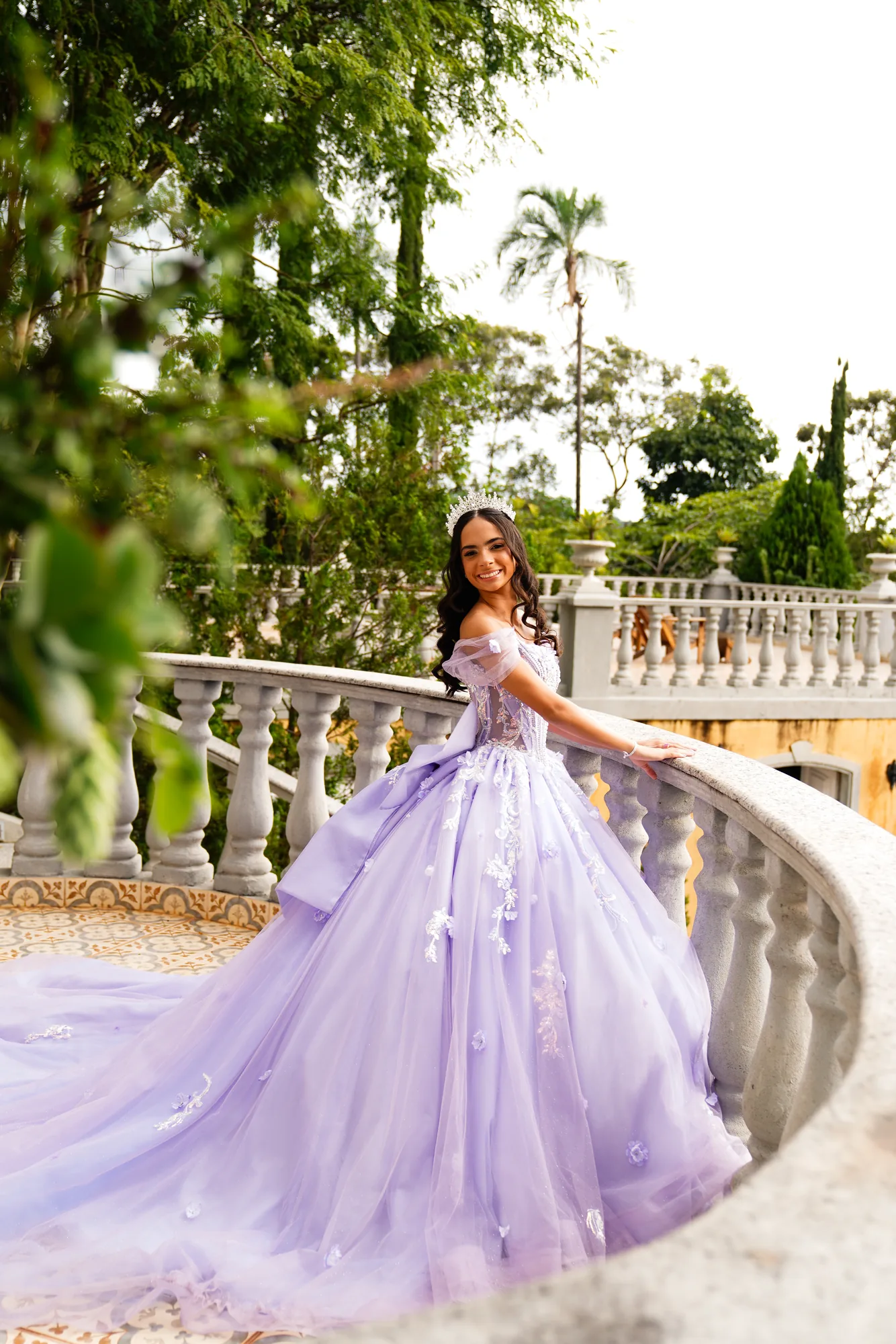 Debutante de vestido lilás na escadaria curva da Villa Giardini, jardim ao fundo