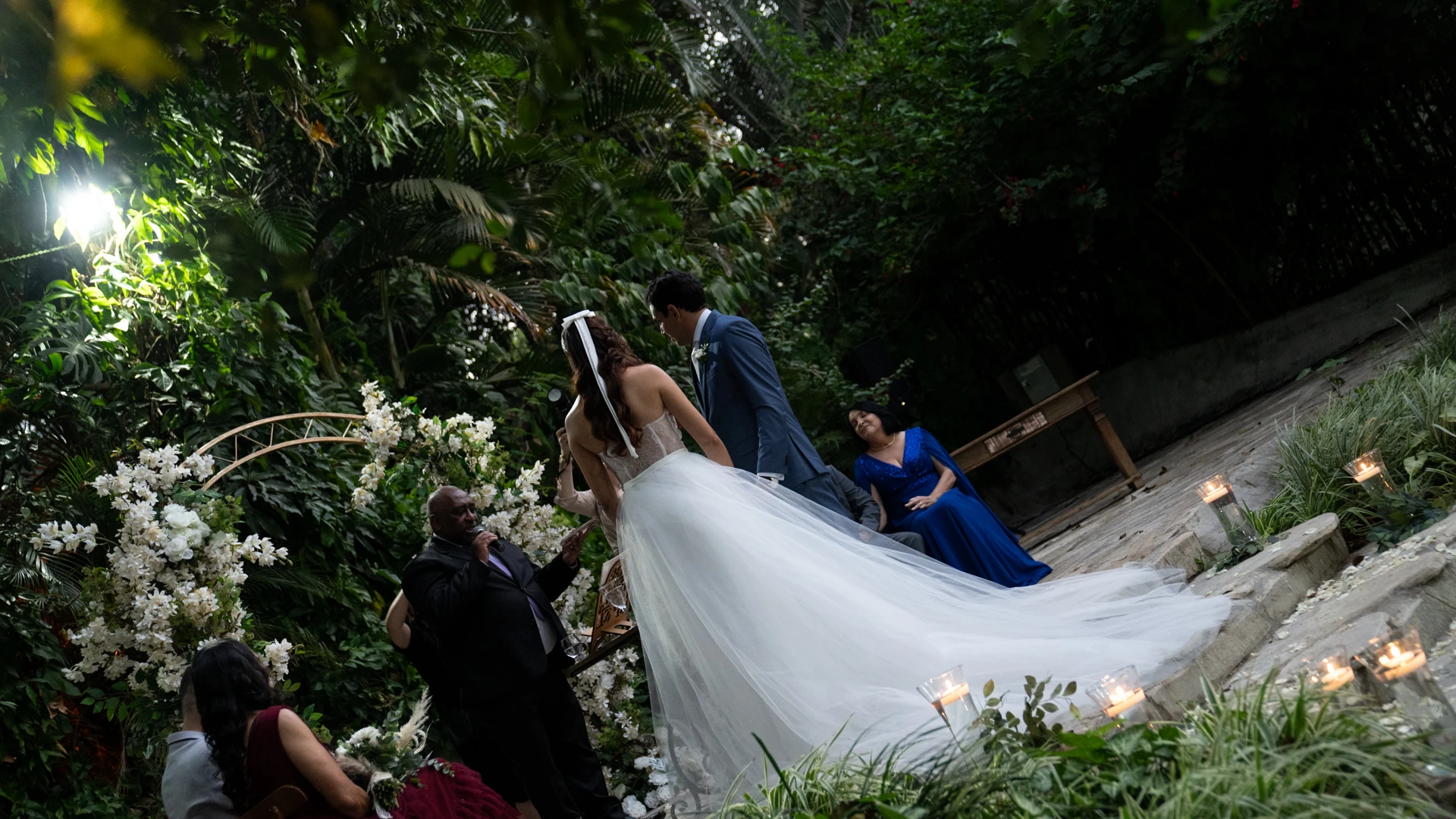 Noiva de véu longo descendo escada em jardim iluminado por velas, ao lado do noivo — cerimônia de casamento ao ar livre em Brasília