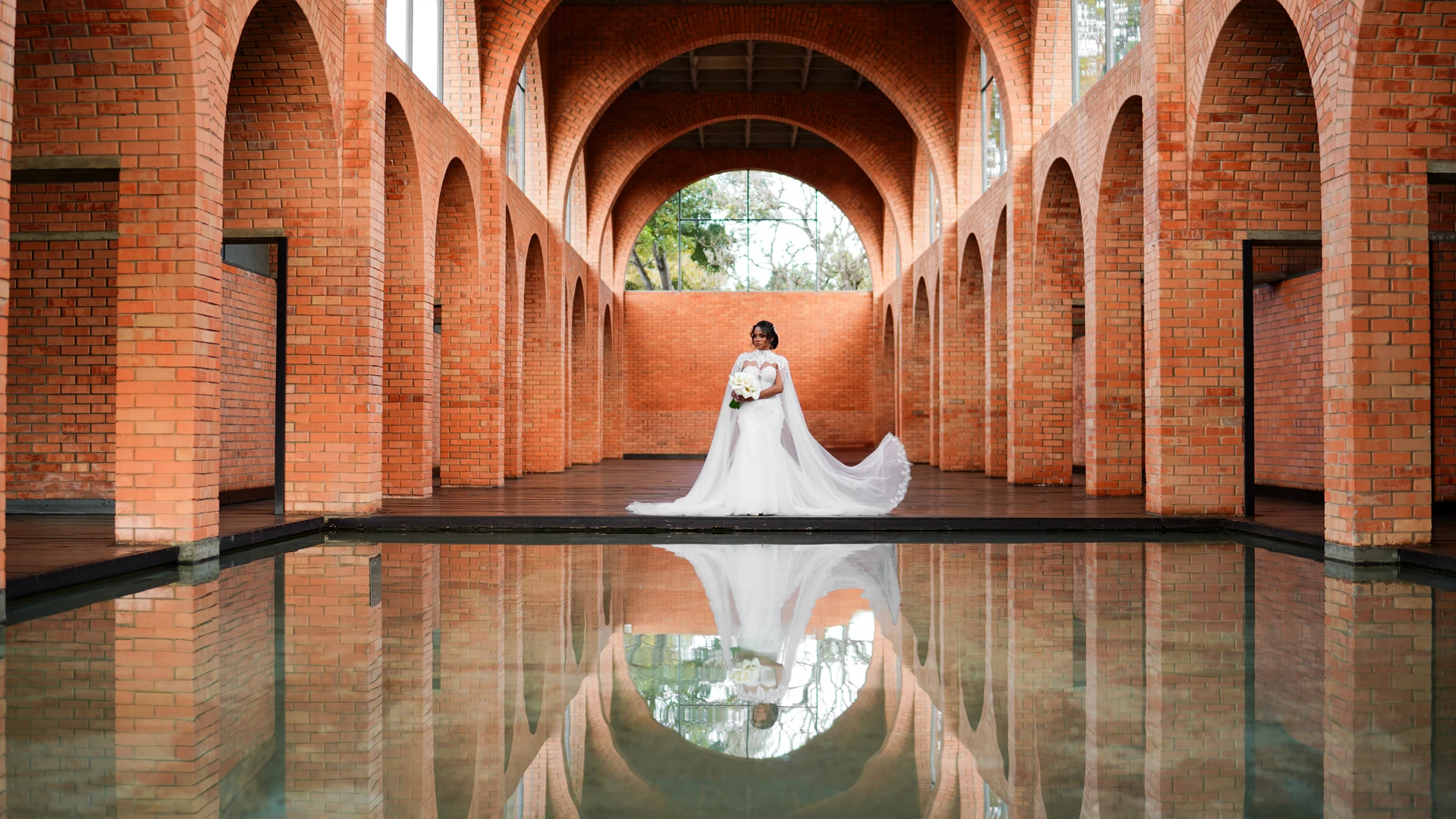 Noiva sozinha refletida na água, em corredor de arcos de tijolo — retrato de casamento editorial em Brasília