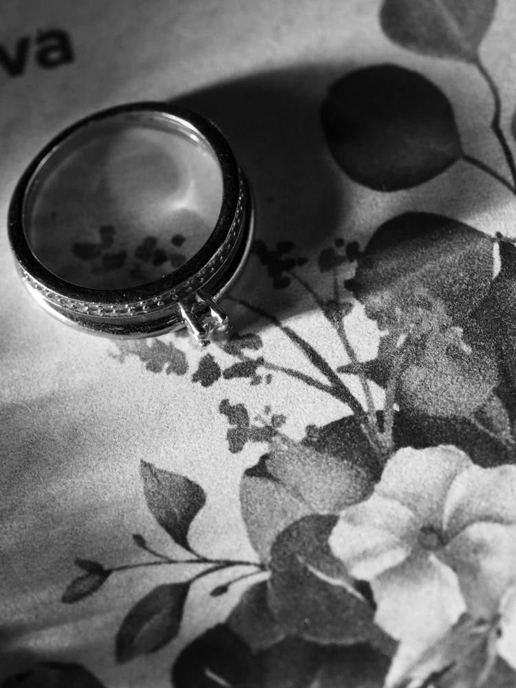 Aliança em caixa aberta sobre papel floral, em preto e branco — still de casamento em Brasília