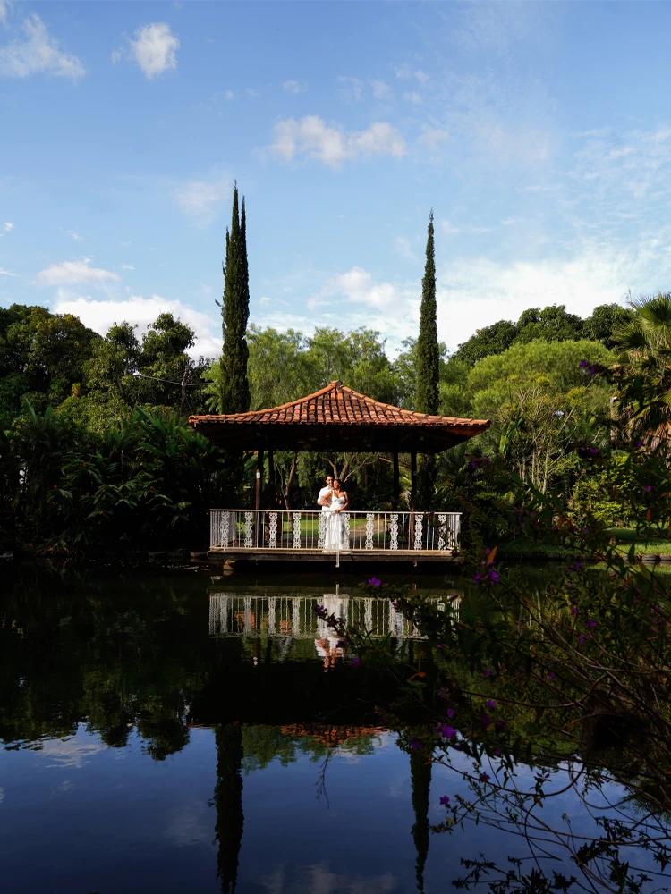 Casal recém-casado abraçado em quiosque à beira de um lago, refletido na água — casamento em Brasília