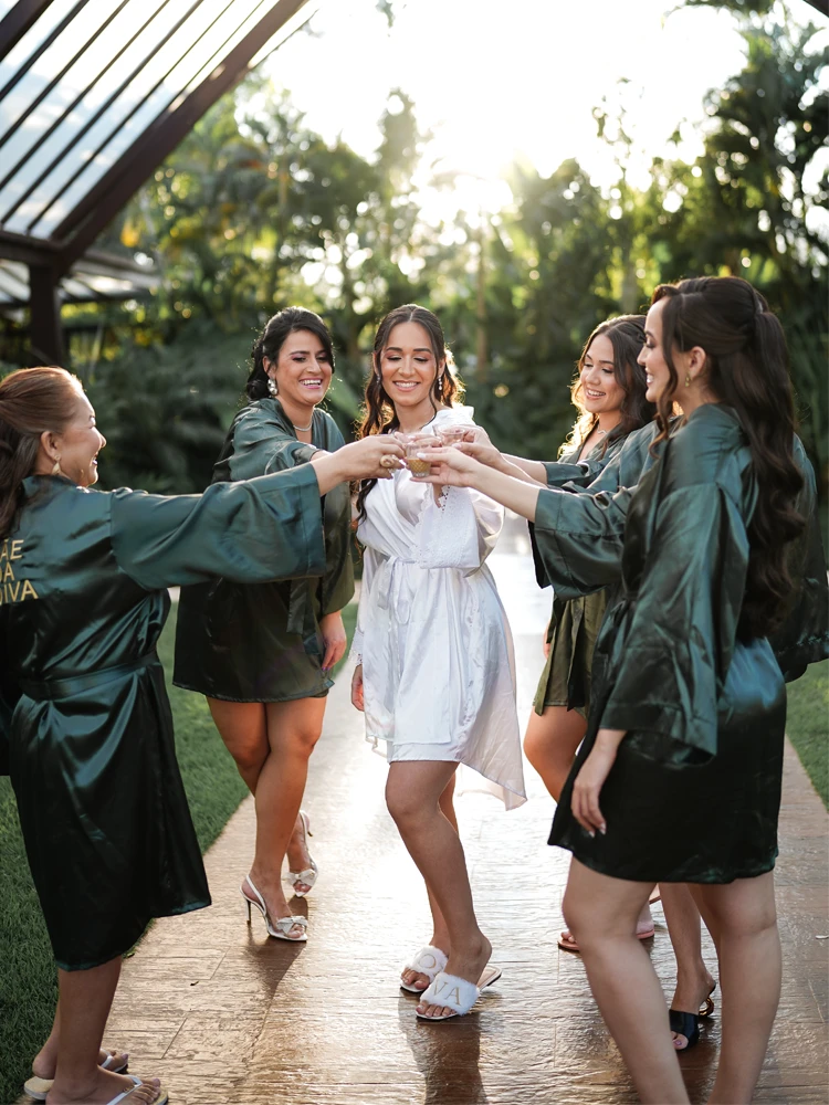 Noiva brindando com as madrinhas em roupão branco, luz do fim de tarde — preparativos de casamento em Brasília