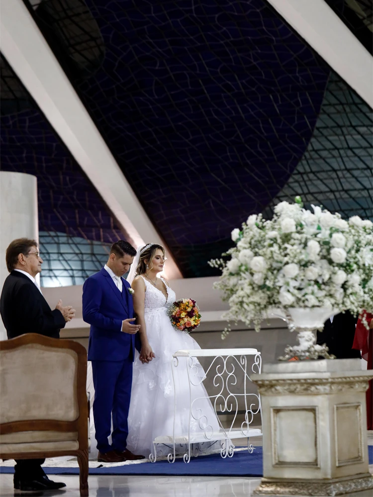 Noivos de mãos dadas diante do altar na Catedral de Brasília, cercados de flores brancas — cerimônia de casamento em Brasília
