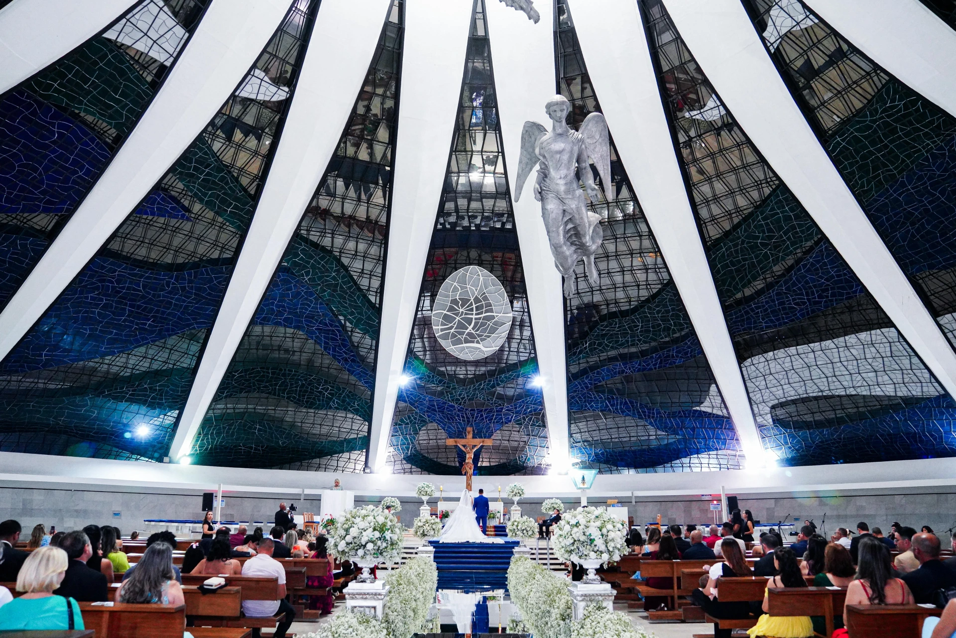 Vista ampla da cerimônia de casamento sob o vitral da Catedral de Brasília, com os convidados nos bancos