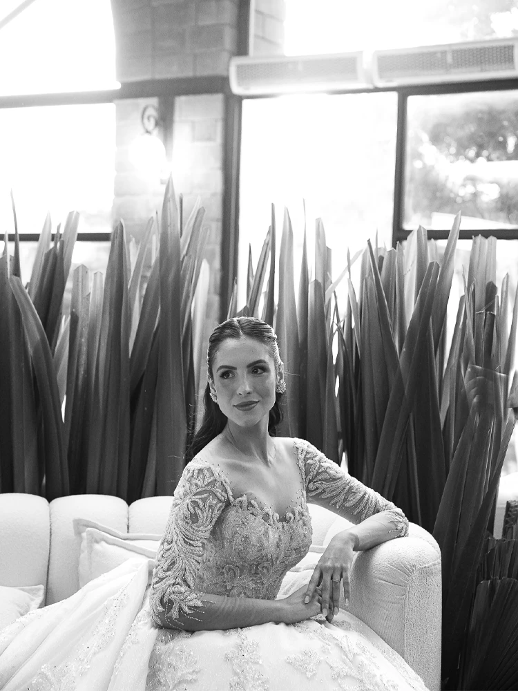 Noiva sentada em sofá branco entre folhagens, em preto e branco — retrato de casamento em Brasília