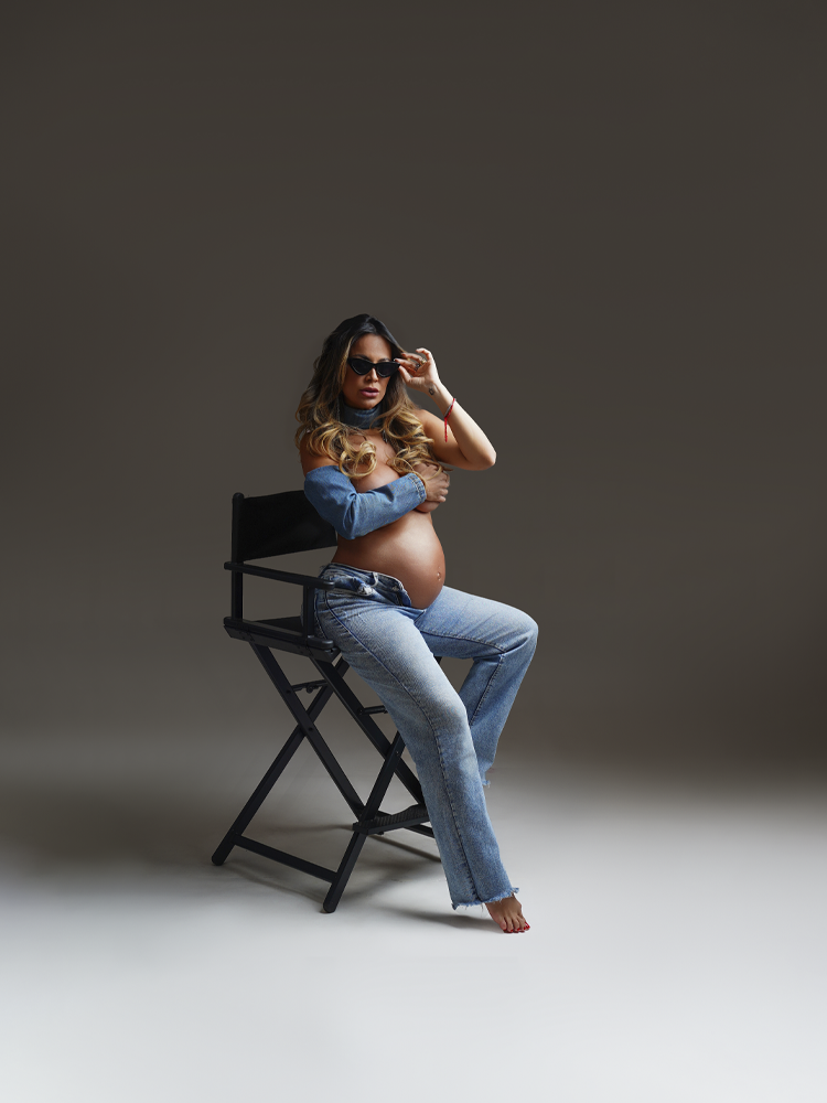 Gestante de jeans e camisa jeans sentada numa cadeira de diretor — ensaio gestante em estúdio, Brasília