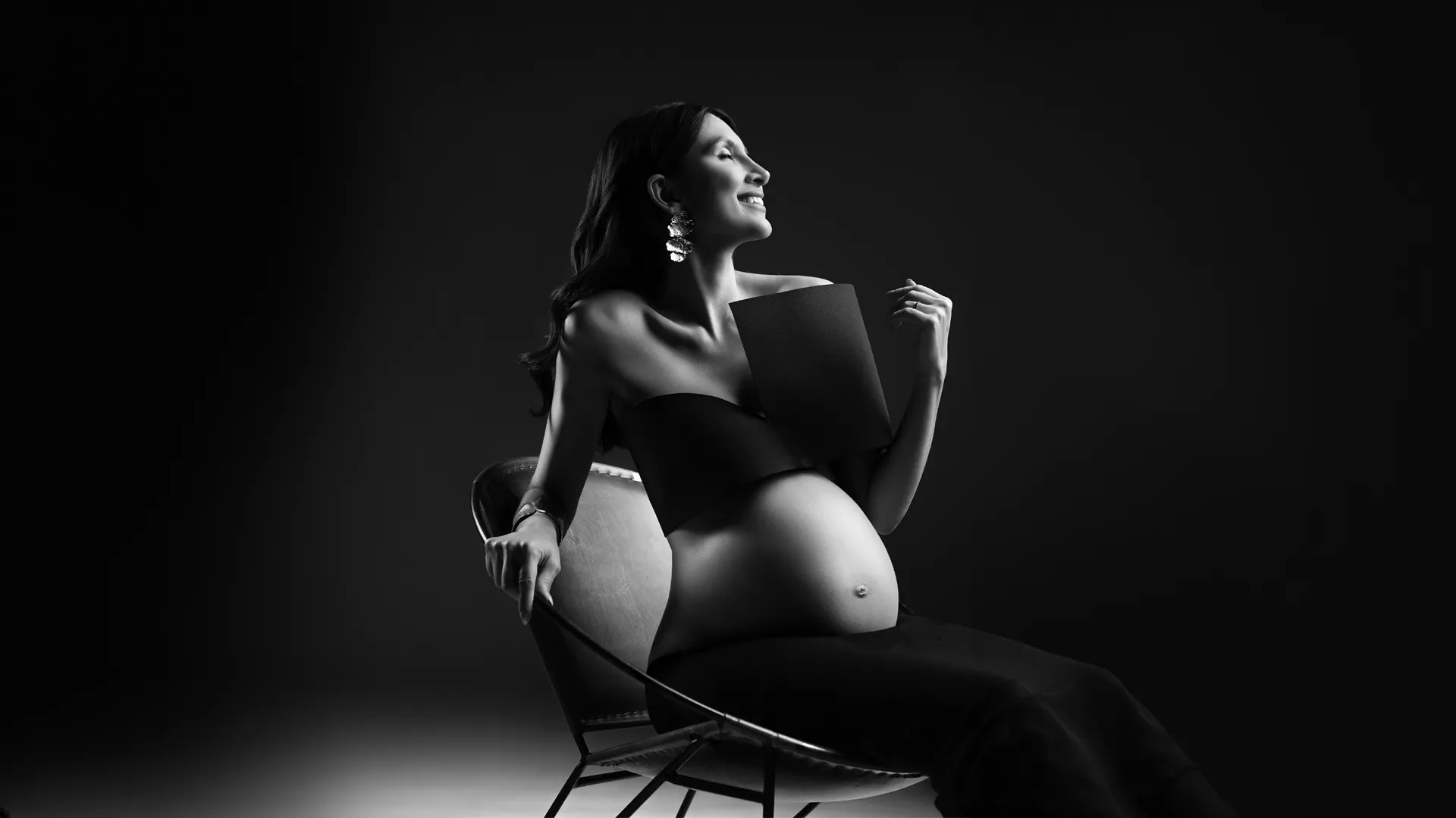 Gestante em retrato editorial preto e branco, sentada numa cadeira — ensaio gestante em Brasília