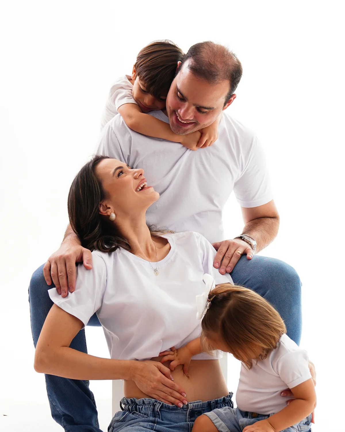 Mãe, pai e irmãozinhos abraçados, de camiseta branca e jeans — sessão de acompanhamento infantil com a família, Brasília